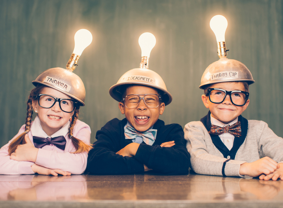 Three kids sit in a classroom setting with a thinking cap on their heads. They are smiling as their light bulbs are lit as the new ideas are flowing. They're wearing cardigans and bow ties. Learning is fun when you have ideas.